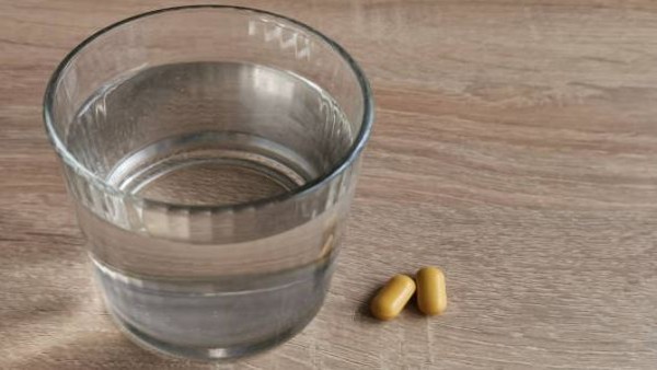 Kapsul vitamin C dan segelas air putih, simbol rutinitas sehat yang perlu dilakukan dengan bijak.