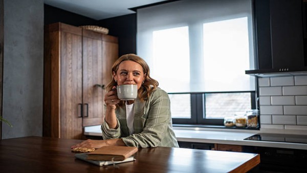 Seorang wanita dewasa menikmati kopi hangat di rumah, menggambarkan momen relaksasi sebelum memulai aktivitas.