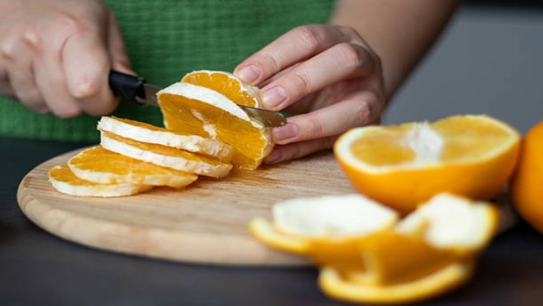 Tangan seorang perempuan sedang memotong jeruk dan grapefruit di dapur, menggambarkan konsumsi buah sehari-hari yang perlu diwaspadai bagi pengguna obat.