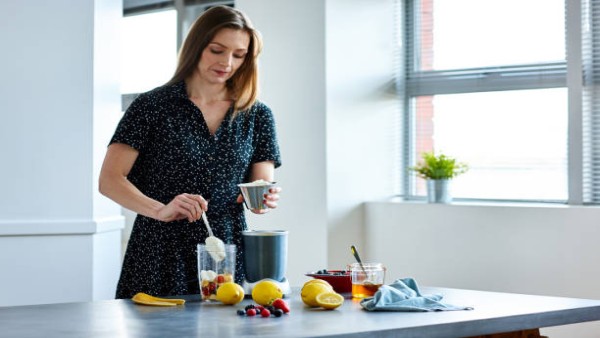 Ilustrasi seorang wanita menyiapkan minuman sehat berbahan serat di dapur sebagai bagian dari gaya hidup sehat.