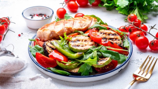 Ilustrasi salad sehat berisi sayuran hijau, sayuran panggang, dan salmon sebagai menu makan siang ramah jantung.