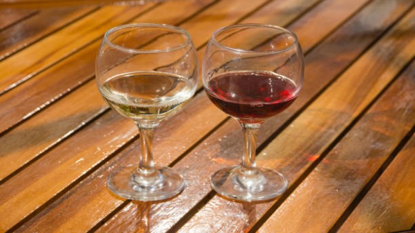 Gelasan anggur merah dan putih di atas meja kayu, menunjukkan pilihan alkohol yang stylish dan sehat dengan konsumsi moderat.