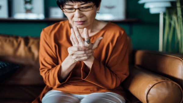 Seorang wanita paruh baya memijat tangannya yang terasa kaku akibat arthritis di pagi hari dengan ekspresi sedikit meringis.