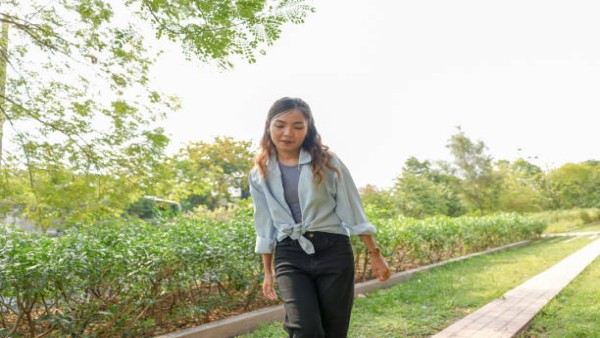 Ilustrasi seorang perempuan sedang berjalan kaki di taman saat sore hari sebagai bagian dari gaya hidup sehat.