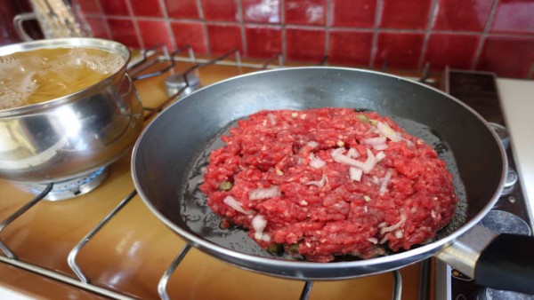 Ilustrasi daging sapi giling yang sedang dimasak di wajan dengan minyak berlebih diserap menggunakan tisu dapur.