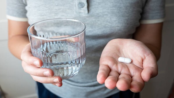 Ilustrasi seseorang memegang tablet metformin dan segelas air minum.